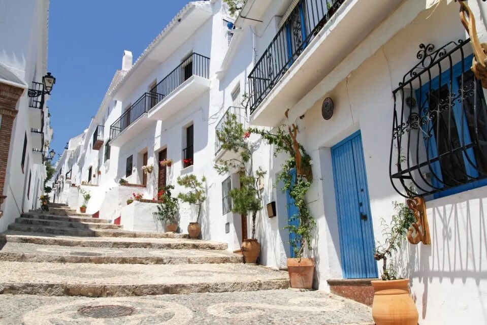 Picturesque street in Frigiliana, Andalusia, Spain, with white buildings and blue doors.