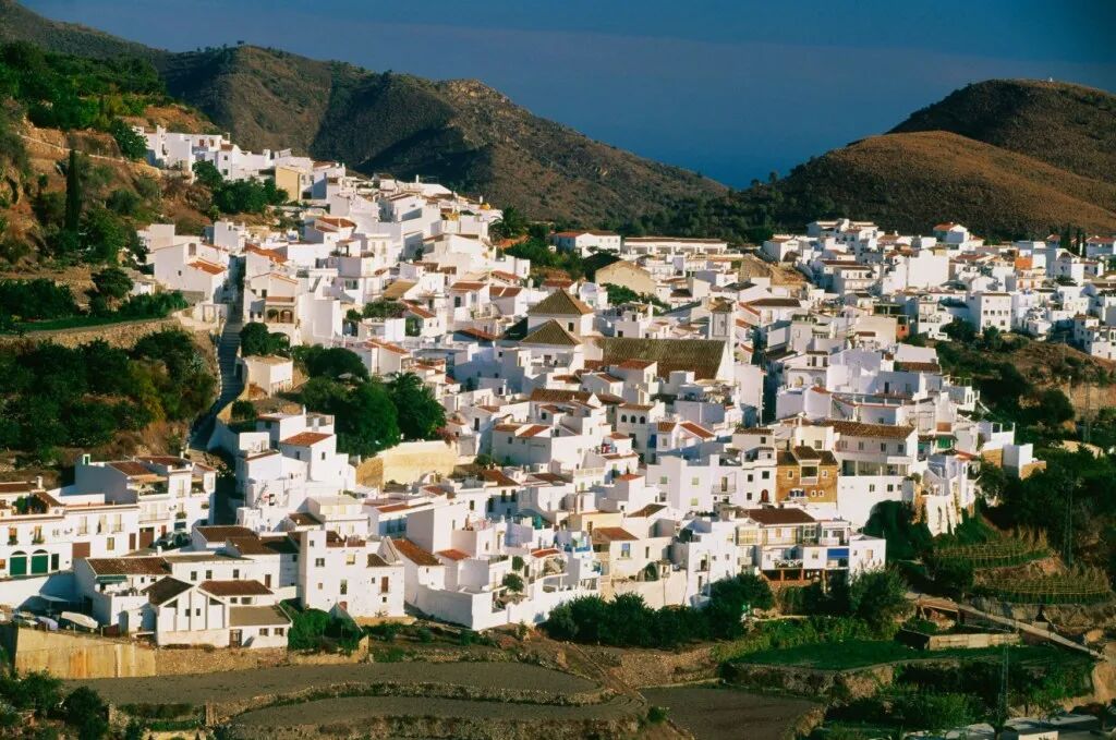 The white village of Frigiliana in Andalusia, Spain, nestled into a hillside with mountains behind it.